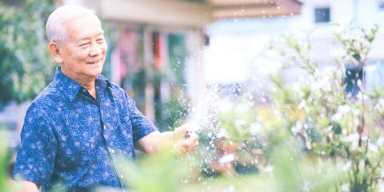 Elderly Man Watering Plants Happily in Garden at Independent Living Facility